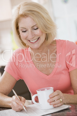 Woman in kitchen with coffee and newspaper smiling