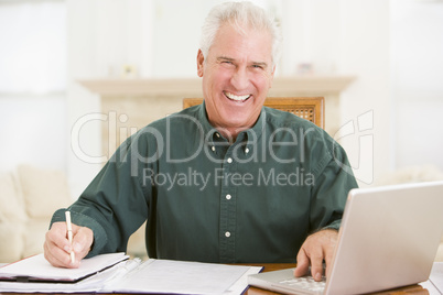 Man in dining room with laptop and paperwork smiling