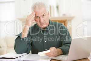 Man in dining room with laptop and paperwork looking frustrated