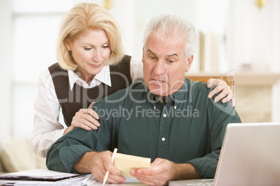 Couple in dining room with laptop and paperwork looking worried