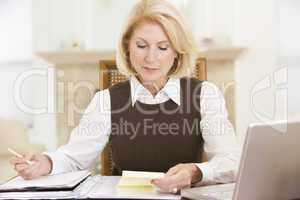 Woman in dining room with laptop and paperwork