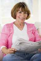 Woman relaxing with newspaper in living room and smiling