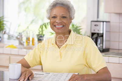 Woman relaxing with newspaper in kitchen and smiling