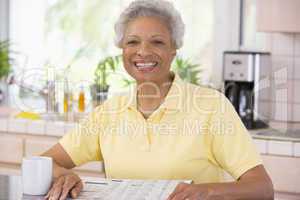 Woman relaxing with newspaper in kitchen and smiling
