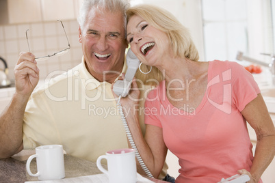 Couple in kitchen using telephone together and laughing