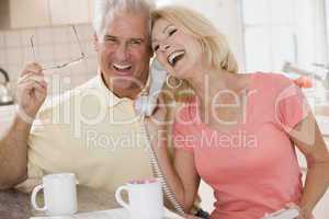 Couple in kitchen using telephone together and laughing