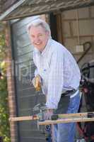 Man at shed sawing wood and smiling