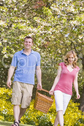 Couple walking outdoors with picnic basket smiling