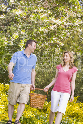 Couple walking outdoors with picnic basket smiling