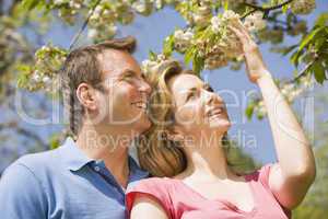Couple standing outdoors holding blossom smiling