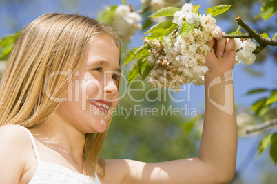 Young girl standing outdoors holding blossom smiling