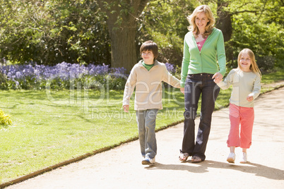 Mother and two young children walking on path holding hands smil