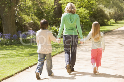 Mother and two young children walking on path holding hands smil