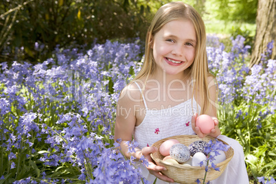 Young girl outdoors holding various eggs in basket smiling