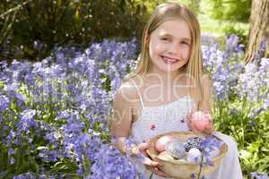Young girl outdoors holding various eggs in basket smiling