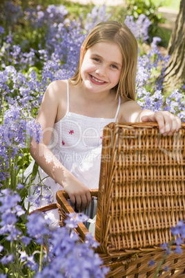 Young girl sitting outdoors with picnic basket smiling