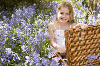 Young girl sitting outdoors with picnic basket smiling