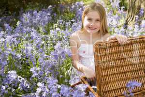 Young girl sitting outdoors with picnic basket smiling