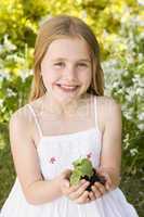 Young girl outdoors holding plant smiling