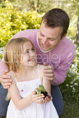 Father and daughter outdoors holding plant smiling