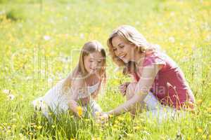Mother and daughter outdoors holding flower smiling