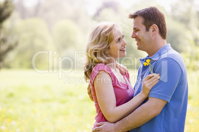 Couple embracing outdoors holding flower smiling