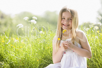 Young girl sitting outdoors holding flower smiling