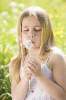 Young girl sitting outdoors blowing dandelion head