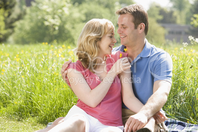 Couple sitting outdoors holding flower smiling