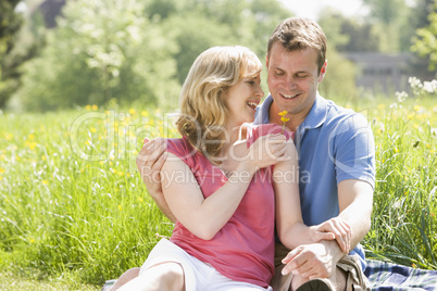 Couple sitting outdoors holding flower smiling