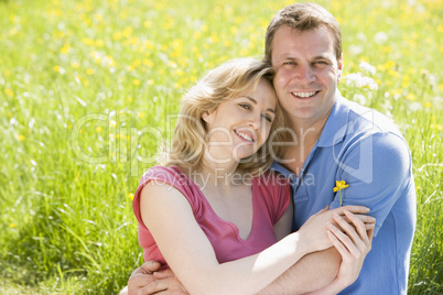 Couple sitting outdoors holding flower smiling