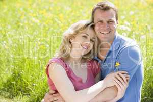 Couple sitting outdoors holding flower smiling