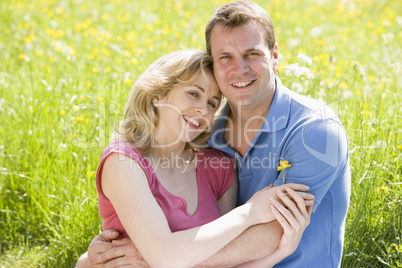 Couple sitting outdoors holding flower smiling