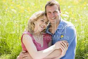 Couple sitting outdoors holding flower smiling