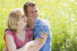 Couple sitting outdoors holding flower smiling