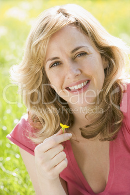 Woman sitting outdoors holding flower smiling