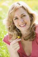 Woman sitting outdoors holding flower smiling