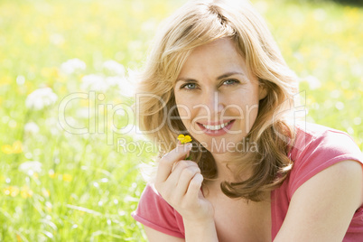 Woman sitting outdoors holding flower smiling