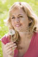 Woman sitting outdoors holding dandelion head smiling