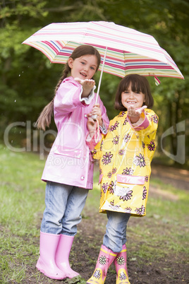 Two sisters outdoors in rain with umbrella smiling