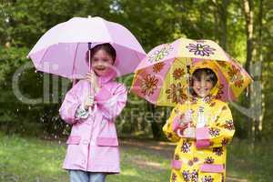 Two sisters outdoors in rain with umbrellas smiling