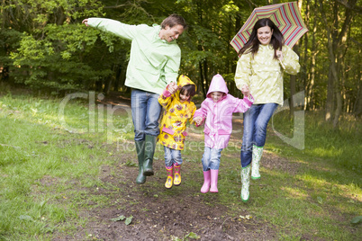 Family outdoors skipping with umbrella smiling