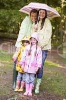 Family outdoors in rain with umbrella smiling