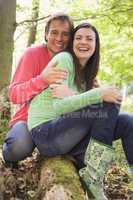 Couple outdoors in woods sitting on log smiling