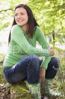 Woman outdoors in woods sitting on log smiling