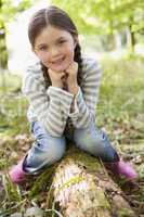 Young girl outdoors in woods sitting on log smiling
