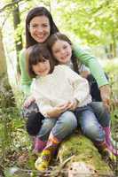 Mother and daughters outdoors in woods sitting on log smiling