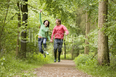 Couple jumping on path holding hands and smiling