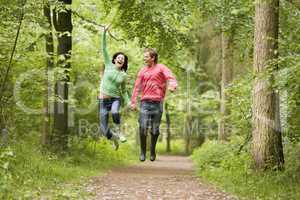 Couple jumping on path holding hands and smiling