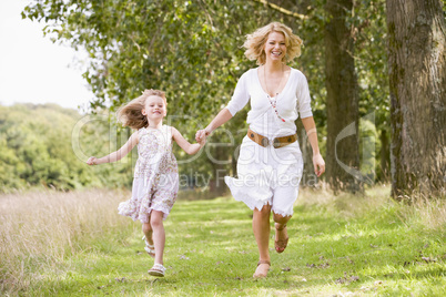 Mother and daughter walking on path holding hands smiling